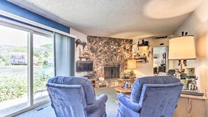 Ein Wohnzimmer mit zwei blauen Sesseln, einem Steinofen, einem Fernseher und Seeblick.