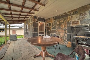 A covered patio area with a round table, stone walls, and a grill. - Unplugged Bryson City Cabin Near Downtown (Bryson City)