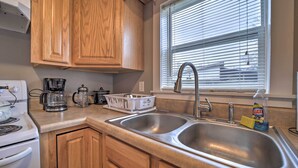 A kitchen with wooden cabinets, a double sink, a coffee maker, and a window with blinds. - Unplugged Bryson City Cabin Near Downtown (Bryson City)