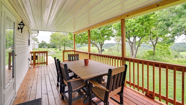 Eine überdachte Veranda mit Holztisch und -stühlen, Blick ins Grüne und einer weißen Holzreling.