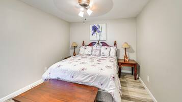 Une chambre à coucher avec un lit en bois, une table de chevet, une lampe, un ventilateur de plafond et un tableau accroché au mur.