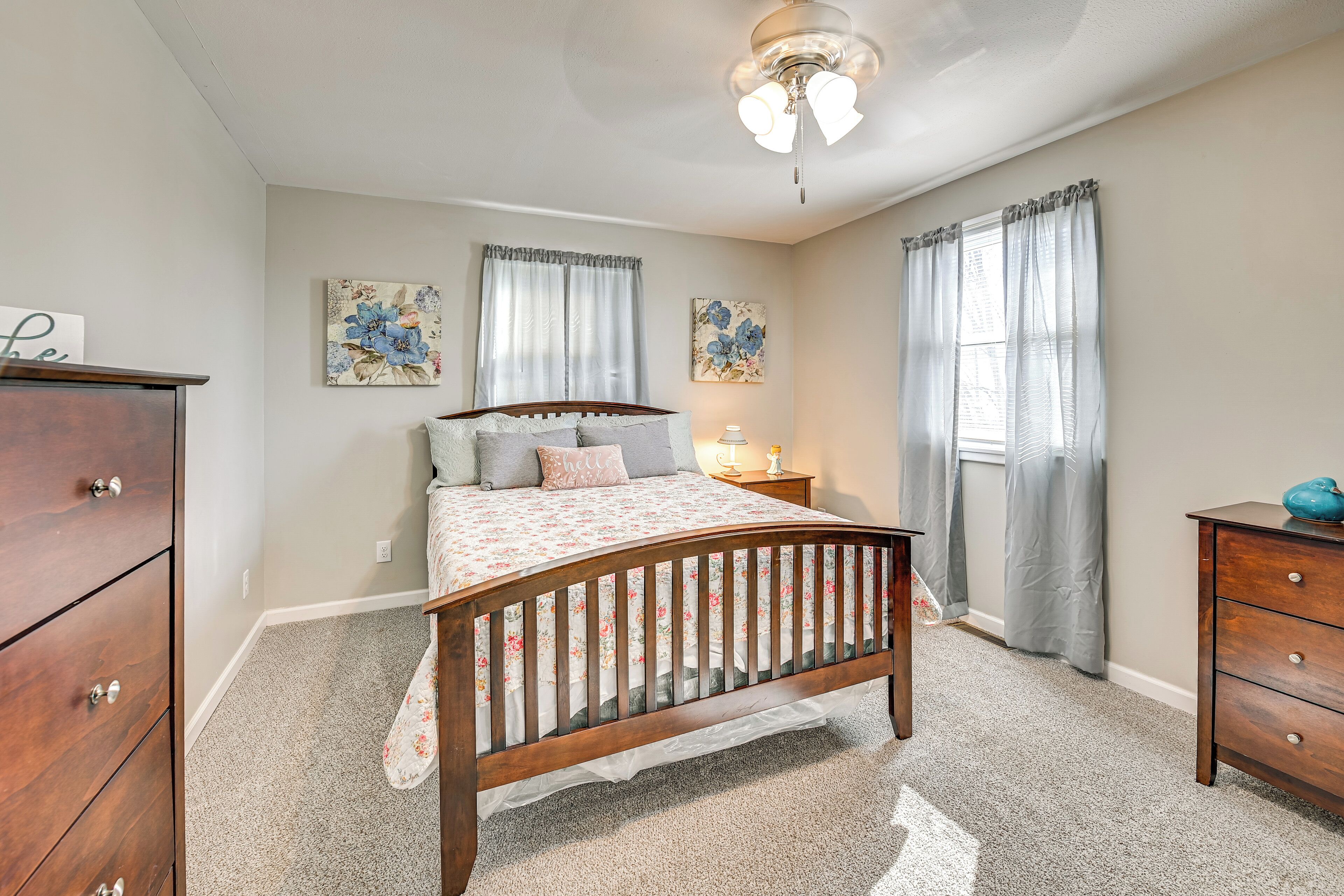 A bedroom with a wooden bed, a nightstand, a dresser, and two floral wall art pieces.