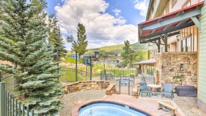 A pool area with a stone wall, outdoor seating, and a view of a town. - Winter Park Condo w/ Mountain Views + Hot Tub (Winter Park)
