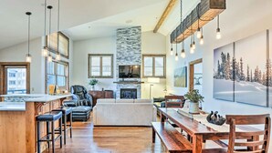 A spacious living area with a fireplace, wooden dining table, and bar stools. - Winter Park Condo w/ Mountain Views + Hot Tub (Winter Park)