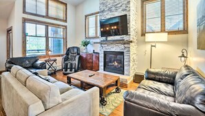 A living room with a fireplace, leather sofas, a coffee table, and large windows with blinds. - Winter Park Condo w/ Mountain Views + Hot Tub (Winter Park)