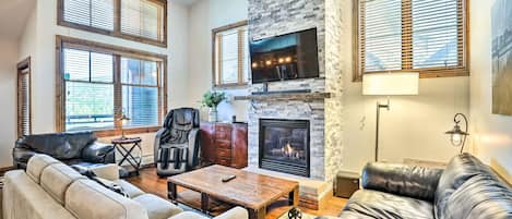 A living room with a fireplace, leather sofas, a coffee table, and large windows with blinds.