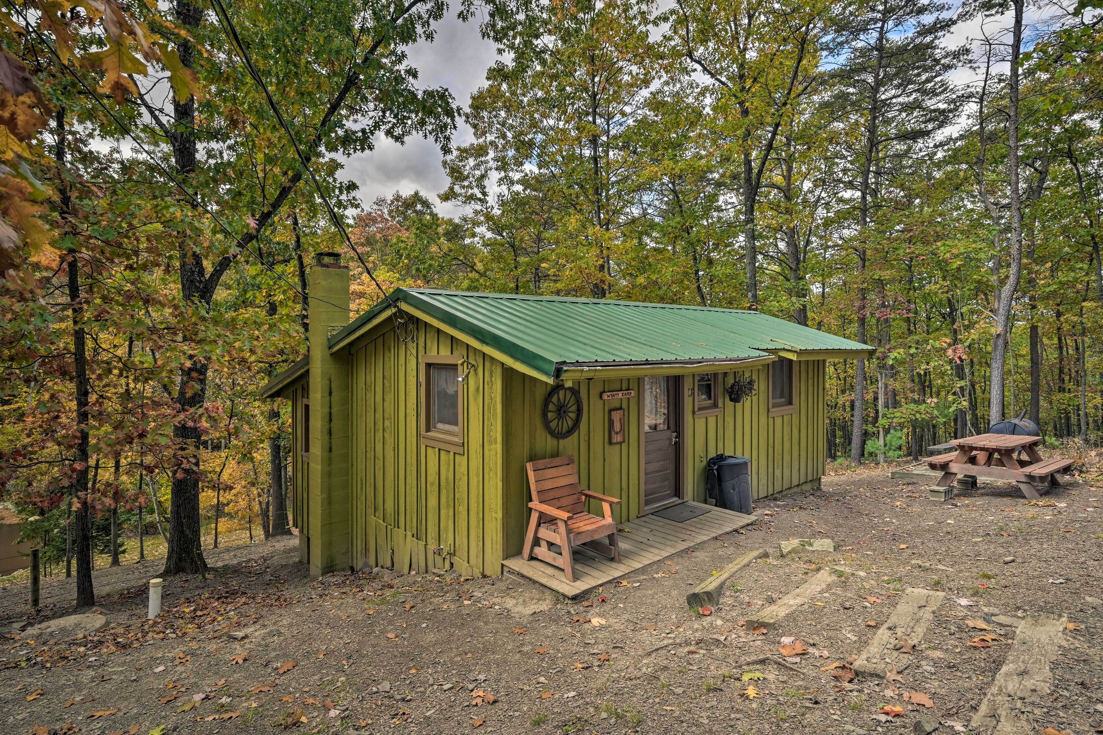 A small cabin with a green roof, a wooden bench outside, and a picnic table nearby.