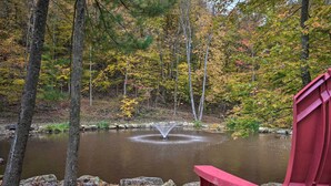 A serene pond with a fountain, surrounded by trees with autumn foliage, and a red chair in the foreground. - 1 Mi to Raystown Lake: 'wyatt Earp Cabin' w/ Deck! (Huntingdon)
