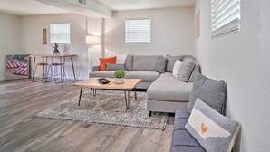 A modern living room with a sofa, coffee table, and a small side table. There is a window with blinds, a lamp, and a plant on the side table. - Updated Knoxville Home w/ Media Room + Patio! (Knoxville)