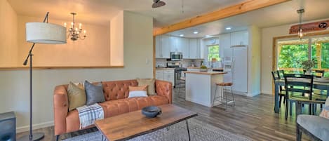 Una sala de estar moderna con un sofá, una mesa de centro y un tapete estampado. Se ve una cocina y comedor al fondo.