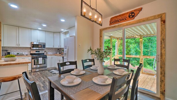 A modern kitchen with white cabinets, stainless steel appliances, and a dining area with a wooden table set for four. - Updated Knoxville Home w/ Media Room + Patio! (Knoxville)