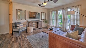 A living room with a sofa, coffee table, and a ceiling fan. There is a window with curtains and a plant on the windowsill. - Updated Knoxville Home w/ Media Room + Patio! (Knoxville)