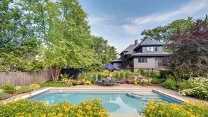 A backyard with a swimming pool, surrounded by lush greenery and a wooden fence.