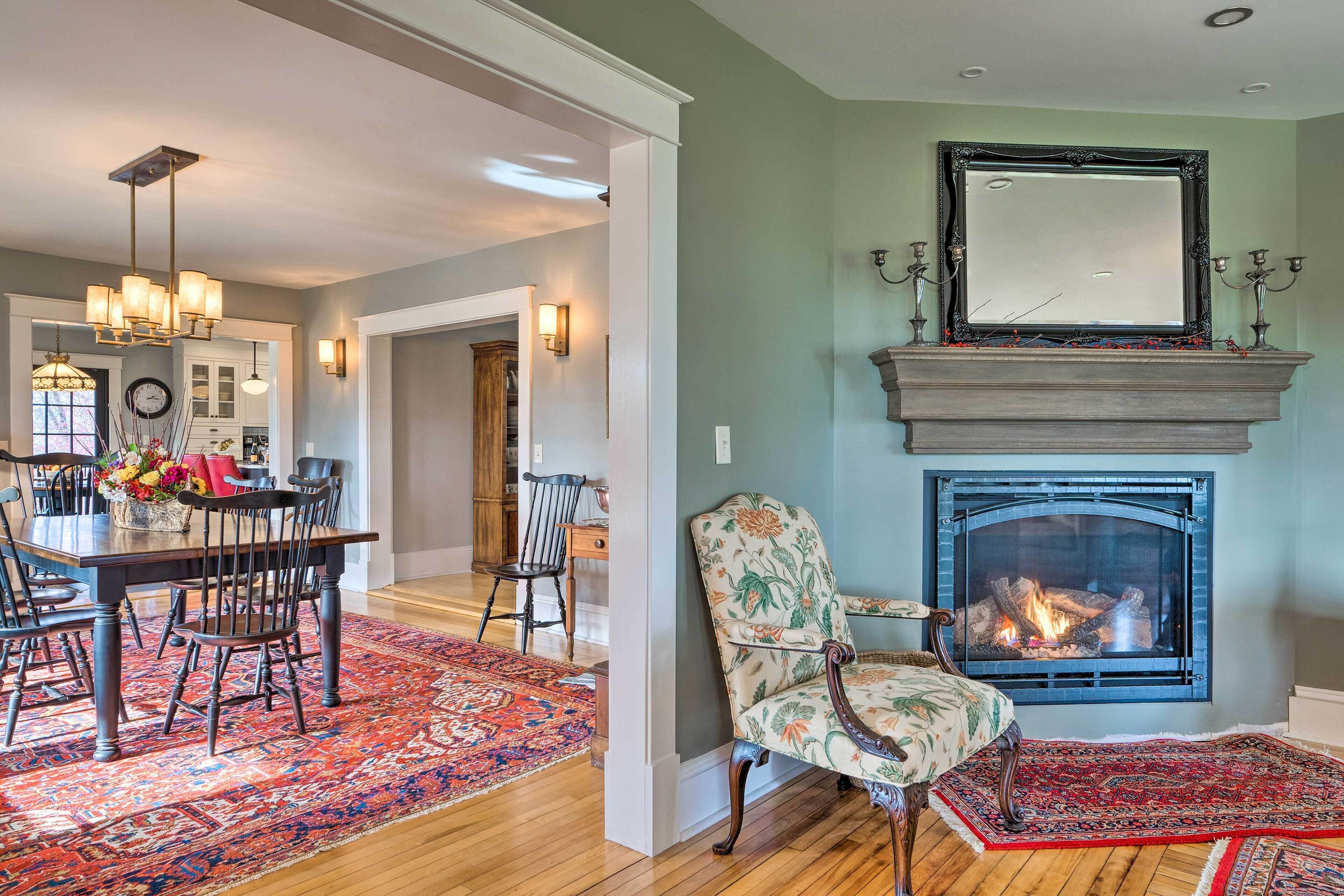 A living room with a fireplace, a dining area with a table and chairs, and a hallway leading to a kitchen.