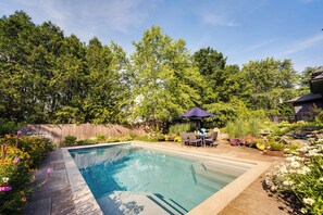 A rectangular swimming pool with a tiled deck, surrounded by lush greenery and a wooden fence. - Upscale Arts + Crafts Bungalow w/ Yard, Pool! (Derby)