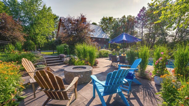 An outdoor patio area with Adirondack chairs, a fire pit, and a blue umbrella.