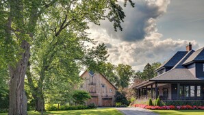 A large wooden barn-style house with a covered porch, surrounded by lush greenery and a well-maintained lawn.