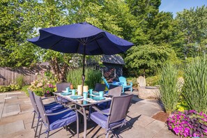 An outdoor patio with a table set for four, surrounded by chairs, and a large umbrella providing shade. - Upscale Arts + Crafts Bungalow w/ Yard, Pool! (Derby)