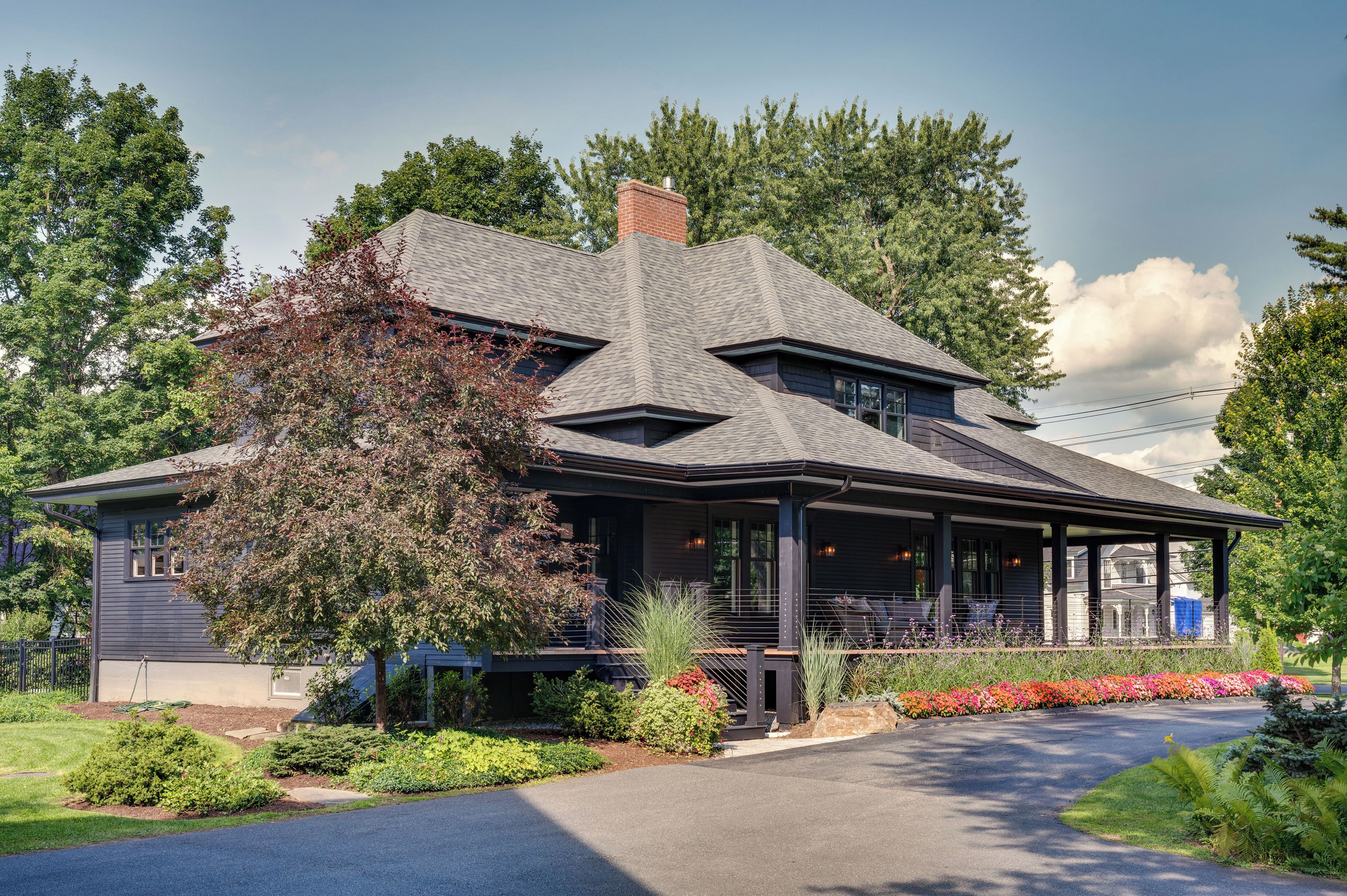 A two-story house with a covered porch, surrounded by a landscaped garden and trees.