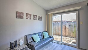 A living room with a gray leather sofa, a small side table, and a window with a view of a wooden fence. - West San Antonio Home w/ Yard: 16 Mi to Dtwn! (San Antonio)