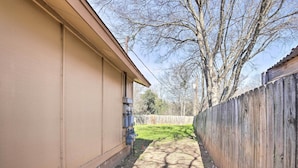 A narrow pathway between a beige building and a wooden fence, with a tree in the background. - West San Antonio Home w/ Yard: 16 Mi to Dtwn! (San Antonio)