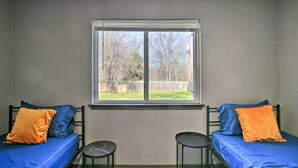 A room with two beds, each with blue and orange pillows, and a window providing a view of a grassy yard and trees. - West San Antonio Home w/ Yard: 16 Mi to Dtwn! (San Antonio)