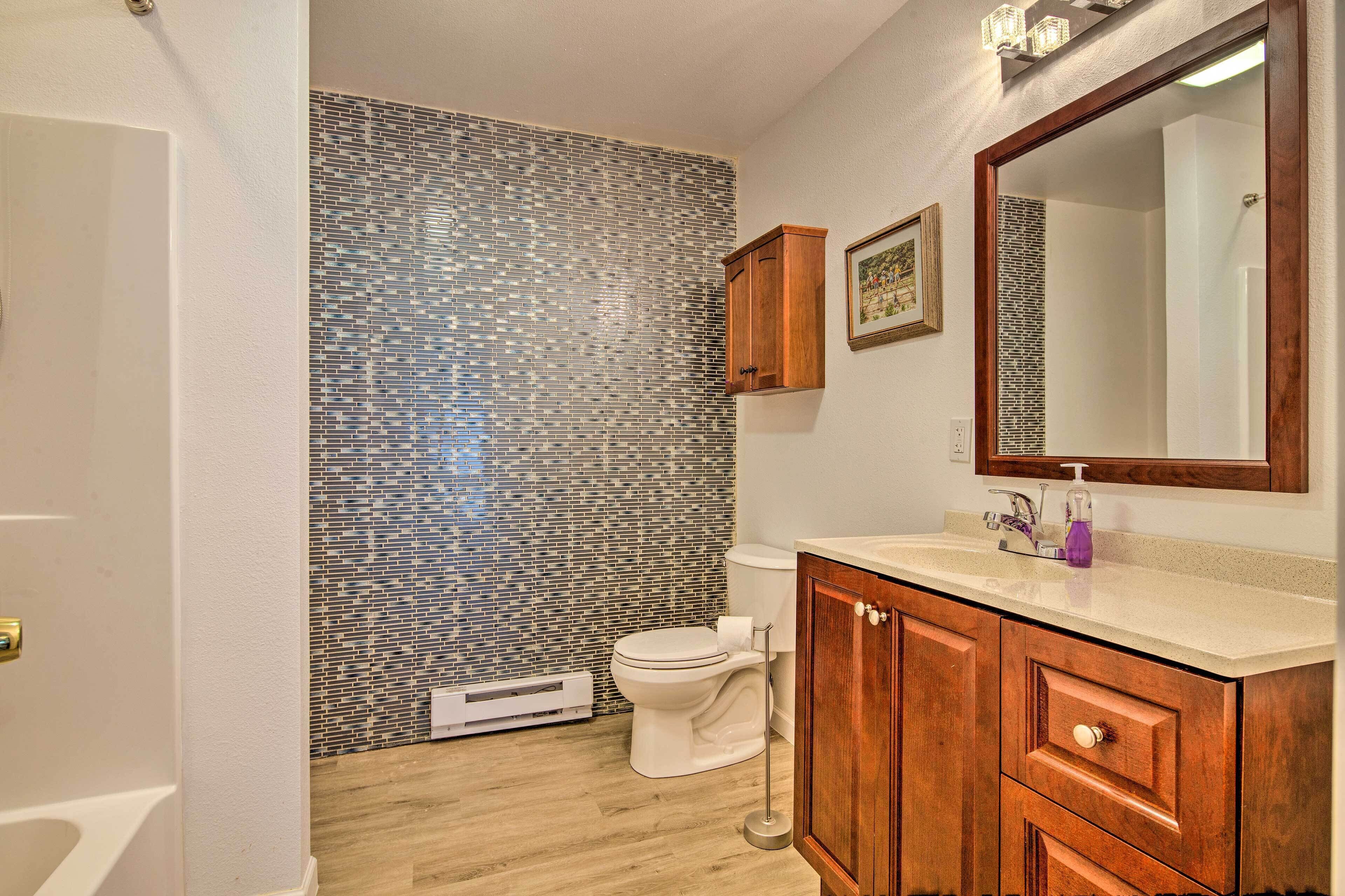 A bathroom with a tiled backsplash, a toilet, a vanity with a mirror, and wooden cabinets.