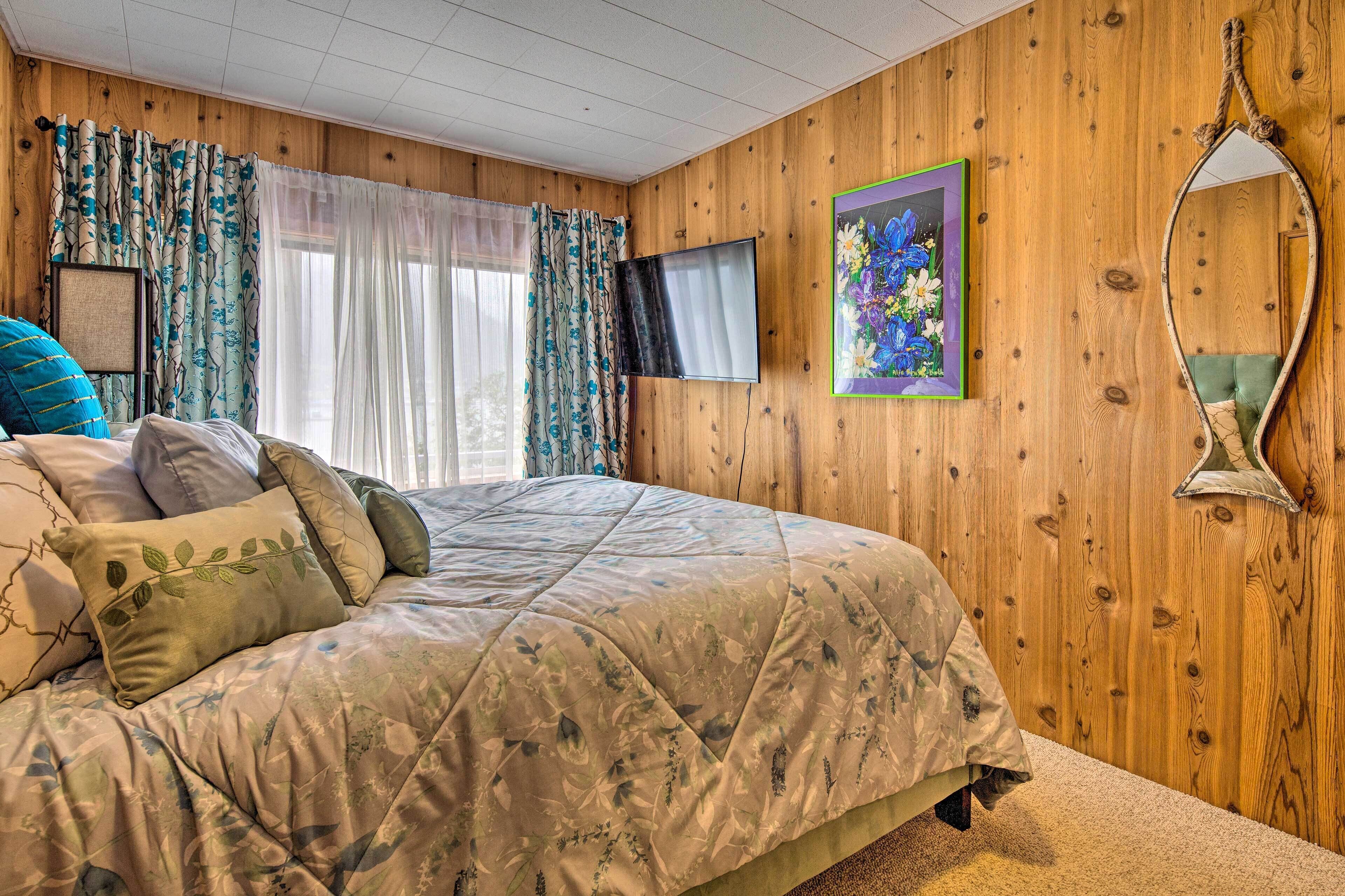 A bedroom with a wooden paneled wall, a bed with a floral bedspread, a television, a framed picture, and a mirror.