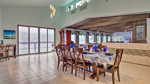 A spacious dining area with a large table, chairs, and a view of a body of water through large sliding doors. - Waterfront House w/ Glacial Views - Near Downtown! (Juneau)