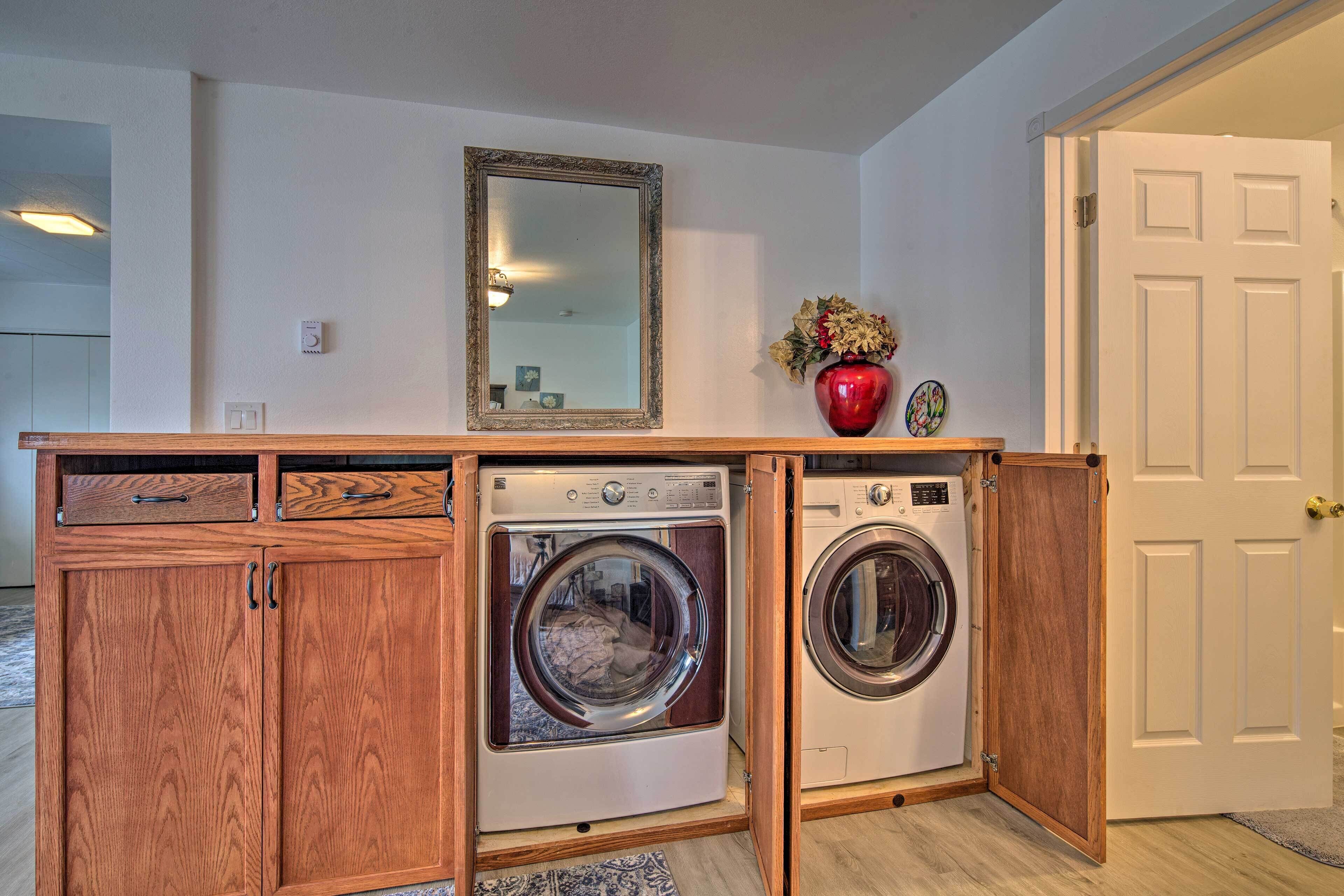 A compact laundry area with two front-loading washers, wooden cabinetry, a mirror, and a vase with flowers.