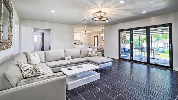 A modern living room with a sectional sofa, a white coffee table, and a large sliding glass door leading to an outdoor patio area. - Waterfront Lake Home w/ Deck - New Renovations! (Willis)