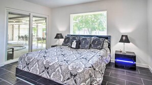 A bedroom with a large bed, two bedside lamps, a nightstand, and a window with a view of greenery. - Waterfront Lake Home w/ Deck - New Renovations! (Willis)