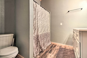A bathroom with a toilet, a shower curtain with a tree pattern, a wooden floor, and a white cabinet. - Waterfront Lake Mille Lacs Lodge w/ Deck + Grill! (Isle)