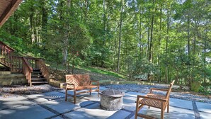 A patio area with wooden chairs and a stone fire pit, surrounded by a forested landscape. - Game Room + Fire Pit: Weaverville Family Home! (Weaverville)