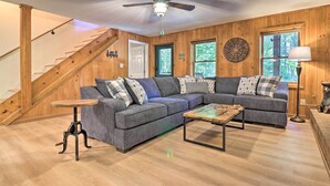 A cozy living room with a wooden staircase, a sectional sofa, a coffee table, and a ceiling fan. - Game Room + Fire Pit: Weaverville Family Home! (Weaverville)