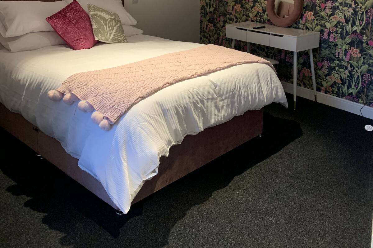 A bedroom with a bed, a nightstand, a wall with floral wallpaper, and a ceiling light.