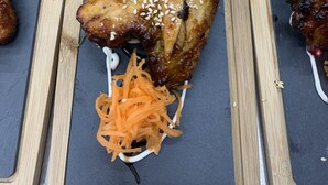 A wooden serving board with grilled chicken wings, lettuce, and carrot slaw. - Stag & Thistle Hotel and Restaurant (Fraserburgh)