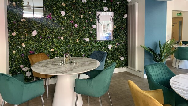 A dining area with a round table, teal and yellow chairs, a green wall with floral decorations, and pendant lighting. - Stag & Thistle Hotel and Restaurant (Fraserburgh)