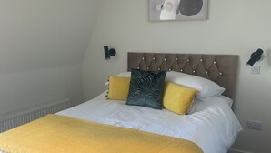 A neatly made bed with a tufted headboard, a yellow throw blanket, and multiple pillows in yellow and green. - Stag & Thistle Hotel and Restaurant (Fraserburgh)