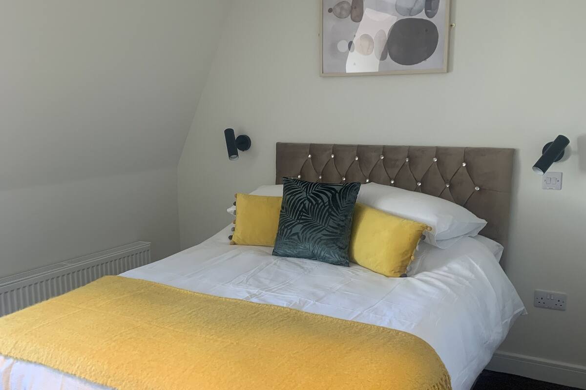 A neatly made bed with a tufted headboard, a yellow throw blanket, and multiple pillows in yellow and green.