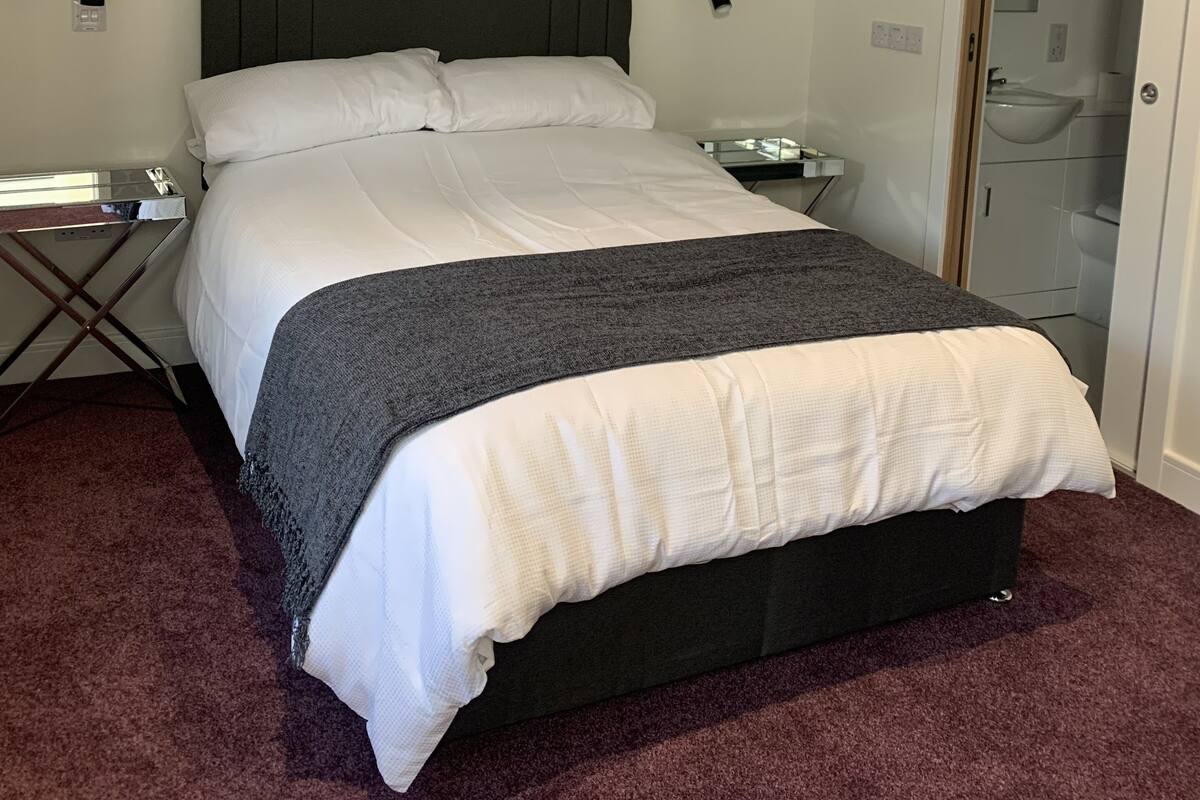 A neatly made bed with a grey and white duvet, a framed picture on the wall, and a small bedside table with a lamp.