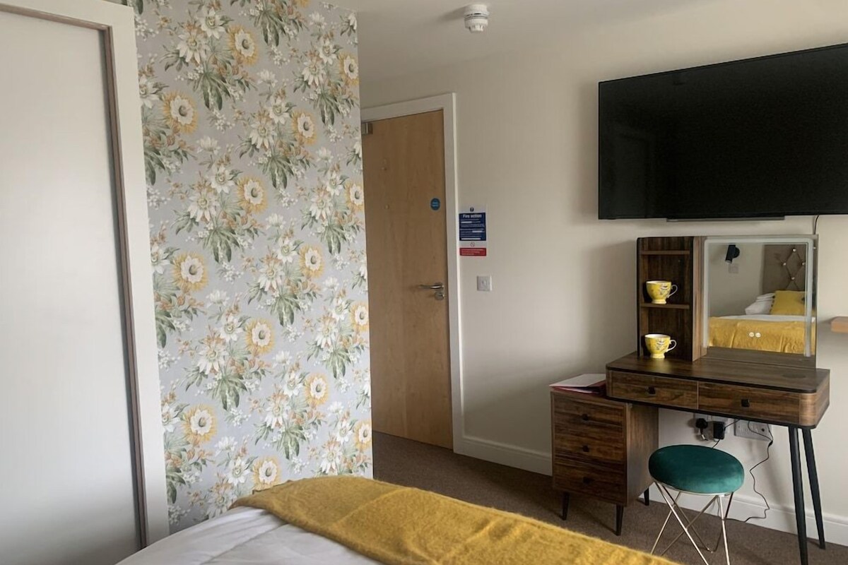 A hotel room with a bed, a desk with a chair, a television, and a door.