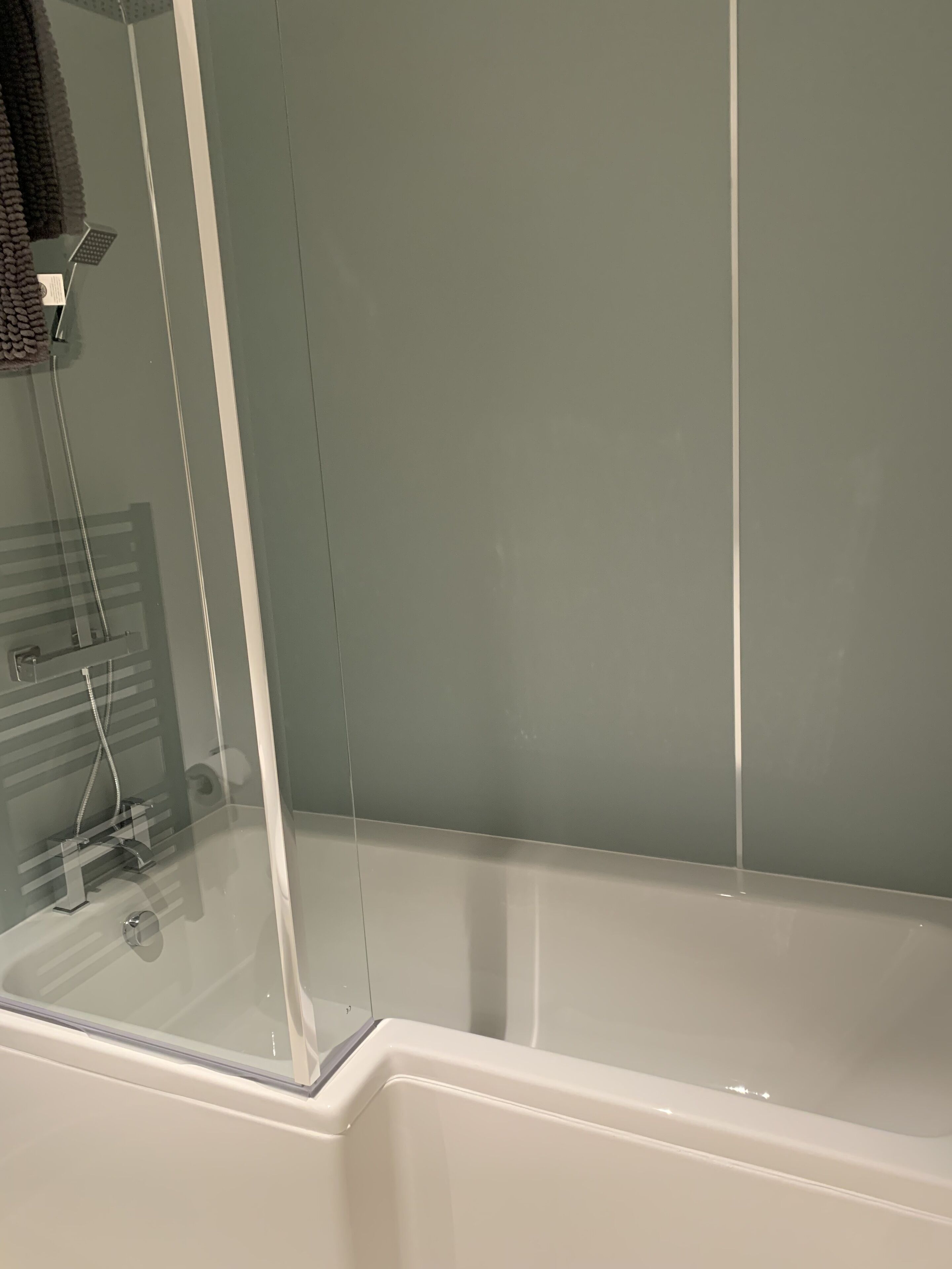 Eine Badewanne mit Glasabtrennung, einer Duschbrause und einem Handtuchhalter.