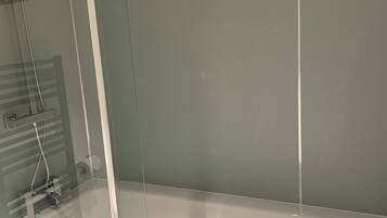 Eine Badewanne mit Glasabtrennung, einer Duschbrause und einem Handtuchhalter.