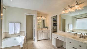 A spacious bathroom with a large bathtub, a vanity with a mirror, and a walk-in closet.