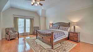 A bedroom with a wooden bed, two chairs, a nightstand, a ceiling fan, and a large window with curtains. - 2,500 Sq Ft Townhome - Walk to Central River Oaks! (Houston)