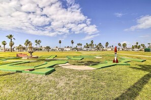 Un campo de mini golf con calles verdes y trampas de arena, rodeado de palmeras y edificios.