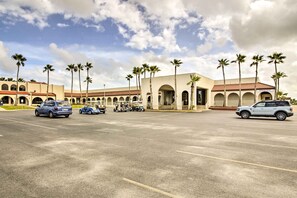 Un estacionamiento con varios coches y carritos de golf, rodeado de edificios con ventanas en arco y palmeras.