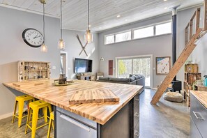 A modern kitchen with a large island, yellow stools, a wooden staircase, and a large window. - Adirondack Cabin Near Whiteface Mountain Resort! (Wilmington)