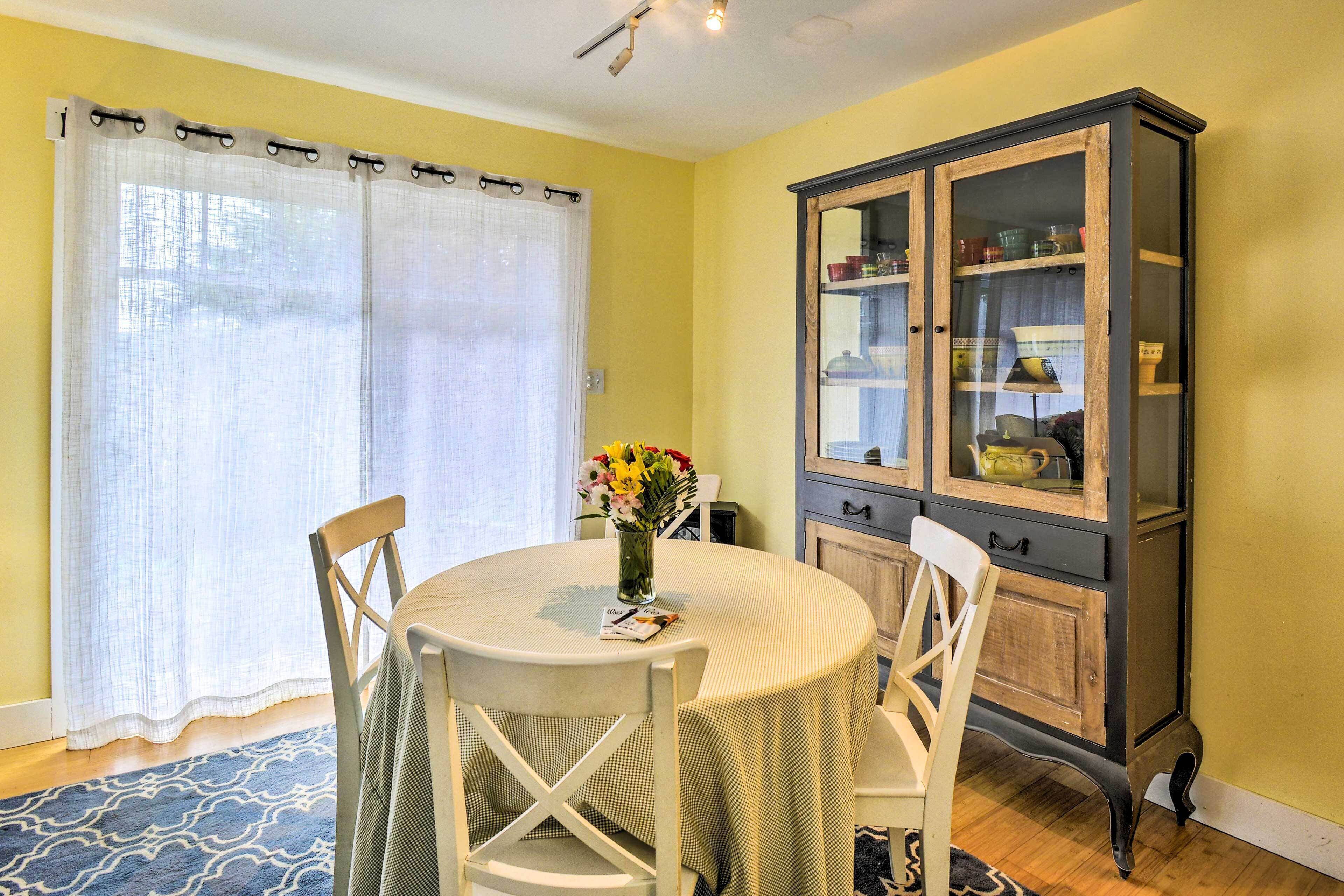 A dining area with a round table, white chairs, a cabinet with glass doors, and a blue patterned rug.